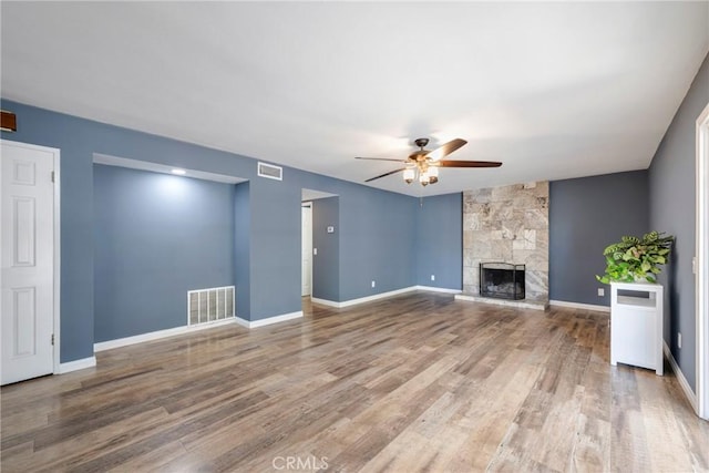 unfurnished living room with wood-type flooring, a stone fireplace, and ceiling fan