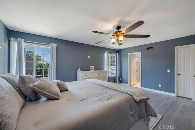 bedroom with multiple windows, ceiling fan, ensuite bathroom, and light wood-type flooring