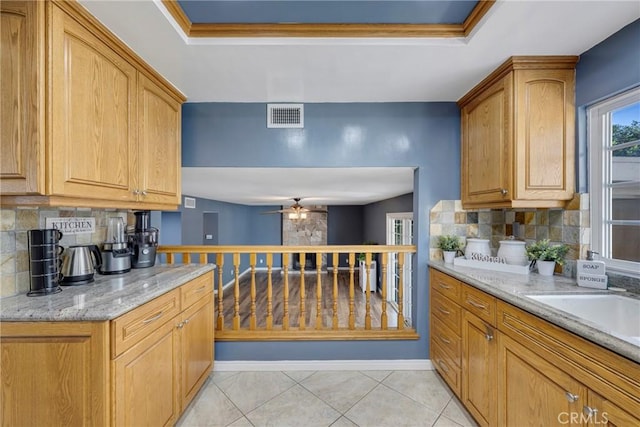 kitchen with decorative backsplash, light stone counters, ceiling fan, and sink