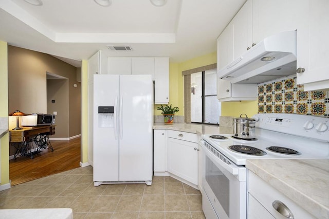 kitchen with white appliances, a tray ceiling, white cabinetry, and light tile patterned floors