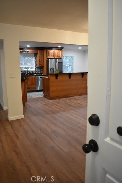 kitchen with kitchen peninsula, hardwood / wood-style floors, backsplash, appliances with stainless steel finishes, and a breakfast bar