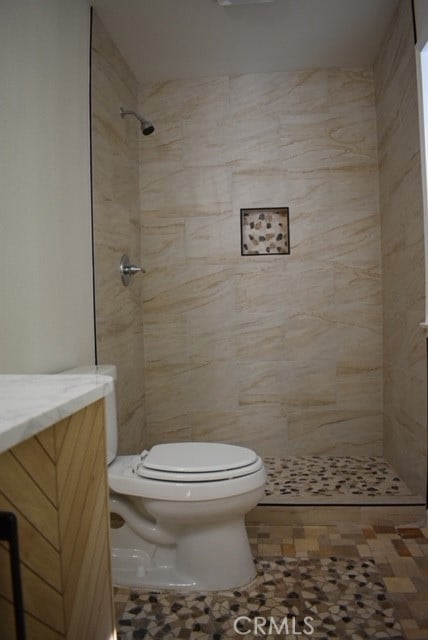 bathroom with vanity, a tile shower, toilet, and tile patterned floors