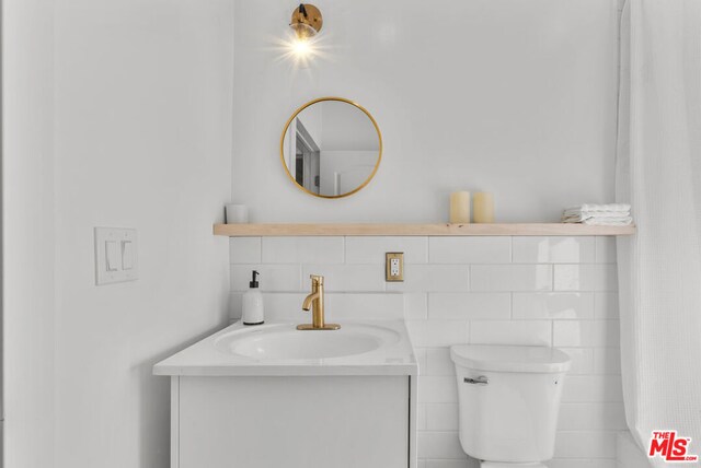 bathroom with vanity, toilet, and tile walls