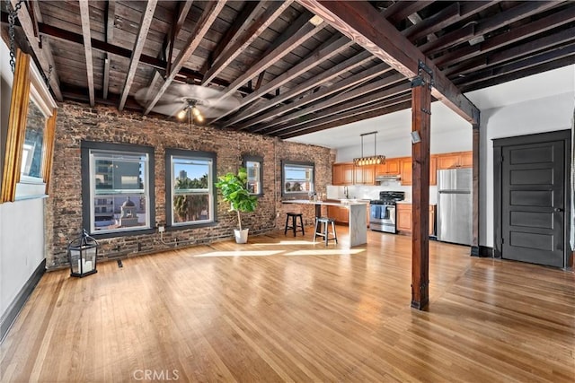 unfurnished living room featuring beamed ceiling, ceiling fan, brick wall, and light hardwood / wood-style flooring