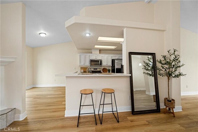 kitchen featuring white cabinets, light hardwood / wood-style flooring, a kitchen bar, kitchen peninsula, and stainless steel appliances