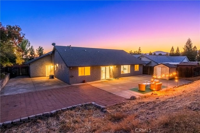 back house at dusk featuring a patio and a storage shed