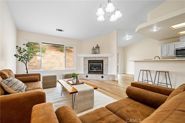 living room with a fireplace, light hardwood / wood-style flooring, lofted ceiling, and an inviting chandelier