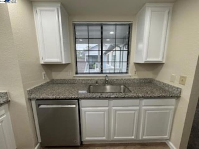 kitchen featuring stainless steel dishwasher, white cabinetry, sink, and dark stone counters