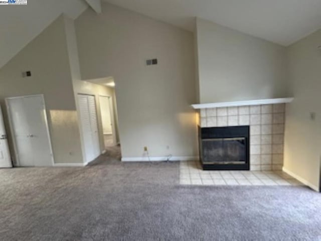 unfurnished living room featuring beamed ceiling, light colored carpet, high vaulted ceiling, and a tiled fireplace