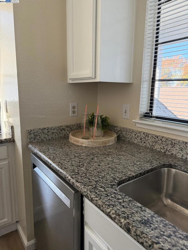 kitchen with white cabinetry, stainless steel dishwasher, dark stone counters, and sink