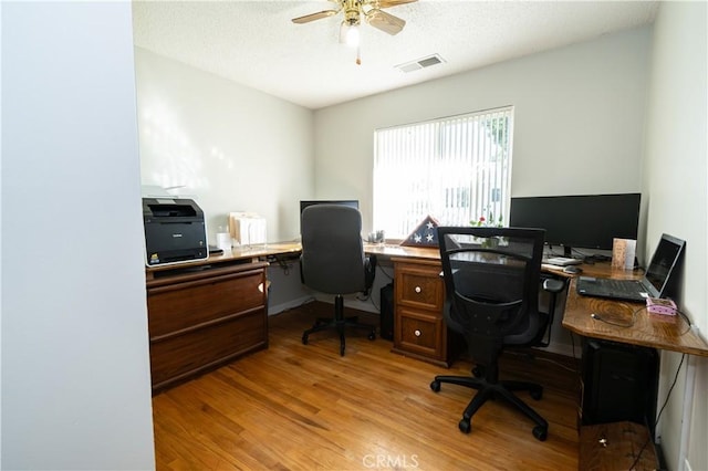 office featuring light wood-type flooring, ceiling fan, visible vents, and a textured ceiling