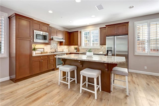 kitchen featuring a kitchen breakfast bar, a kitchen island, appliances with stainless steel finishes, light hardwood / wood-style floors, and light stone counters