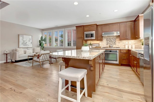 kitchen with decorative backsplash, appliances with stainless steel finishes, light stone counters, light hardwood / wood-style floors, and a kitchen island