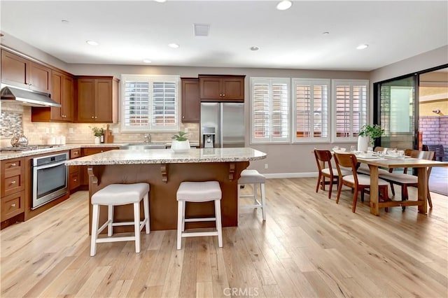 kitchen with light stone counters, a center island, stainless steel appliances, and light wood-type flooring