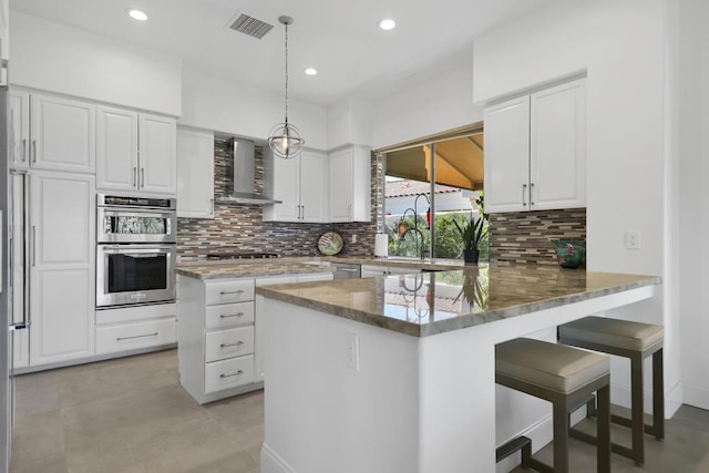 kitchen featuring kitchen peninsula, white cabinets, tasteful backsplash, and wall chimney exhaust hood