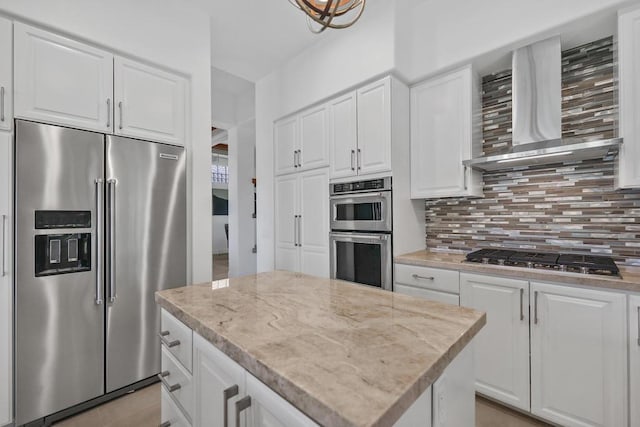 kitchen featuring white cabinetry, a kitchen island, stainless steel appliances, and wall chimney range hood