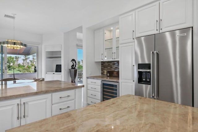 kitchen with light stone countertops, tasteful backsplash, high end fridge, white cabinets, and wine cooler