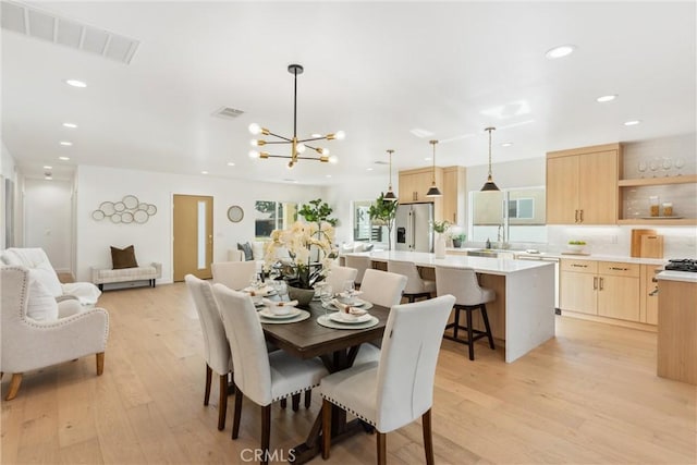 dining area featuring sink, light hardwood / wood-style flooring, and an inviting chandelier