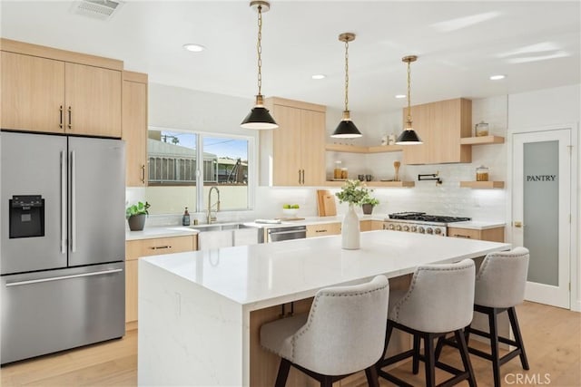 kitchen featuring a kitchen island, light wood-type flooring, decorative light fixtures, and appliances with stainless steel finishes