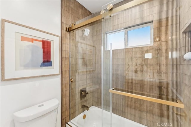 bathroom featuring toilet and bath / shower combo with glass door