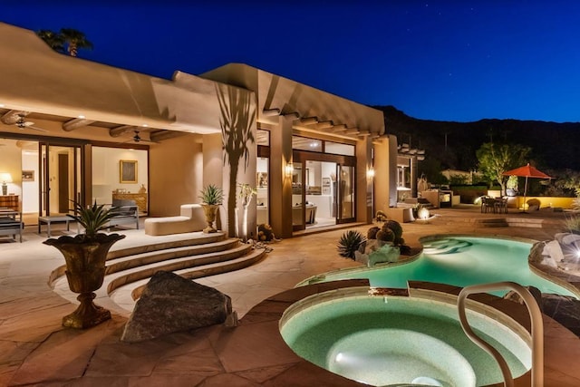 patio at night featuring ceiling fan and a swimming pool with hot tub