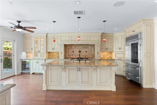 kitchen featuring decorative light fixtures, cream cabinetry, and an island with sink