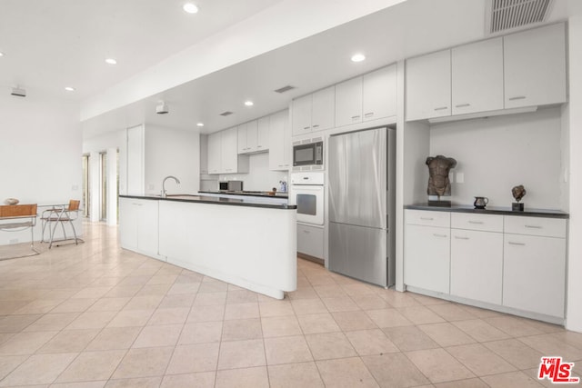 kitchen with oven, stainless steel fridge, white cabinets, and built in microwave