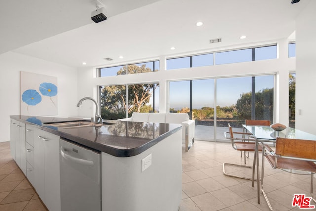 kitchen featuring sink, light tile patterned flooring, dishwasher, white cabinets, and a kitchen island with sink