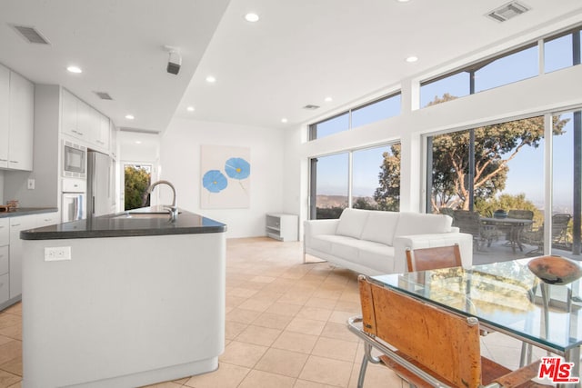 kitchen with white oven, stainless steel microwave, a healthy amount of sunlight, sink, and white cabinets