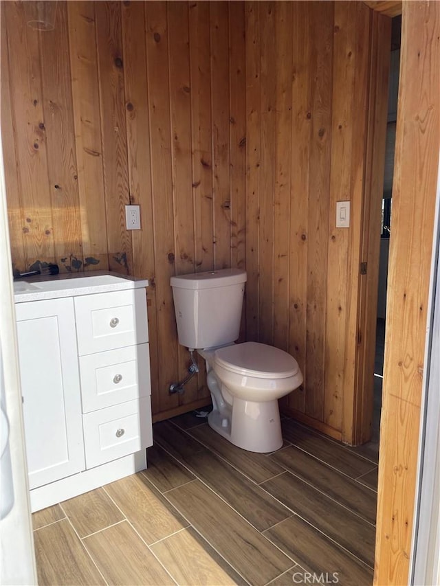 bathroom with vanity, toilet, and wood walls