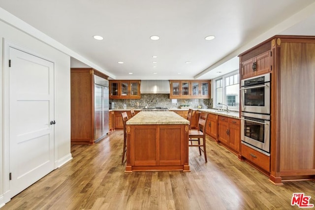 kitchen with a breakfast bar, wall chimney range hood, light hardwood / wood-style floors, a kitchen island, and stainless steel appliances