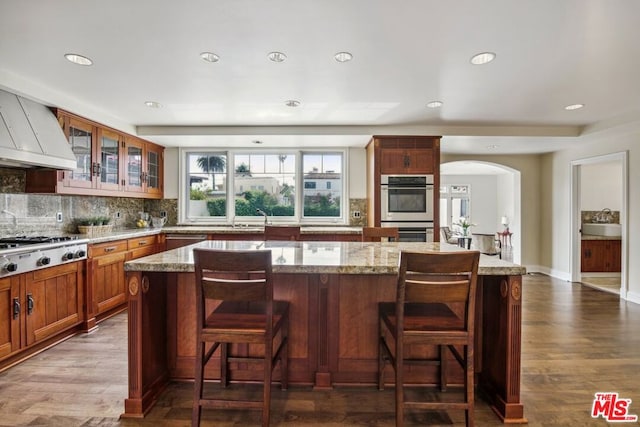 kitchen featuring sink, a center island, dark wood-type flooring, light stone counters, and appliances with stainless steel finishes