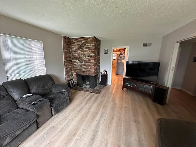 living room with a brick fireplace, a textured ceiling, visible vents, and wood finished floors