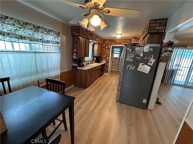 kitchen with brick wall, light wood-style flooring, freestanding refrigerator, light countertops, and a sink