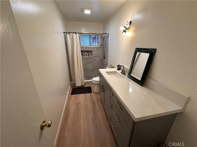 full bathroom featuring toilet, vanity, wood finished floors, tiled shower, and baseboards