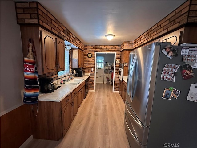 kitchen with light wood-style floors, freestanding refrigerator, light countertops, and brick wall