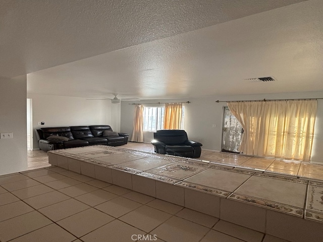 unfurnished living room with ceiling fan, a textured ceiling, and tile patterned flooring