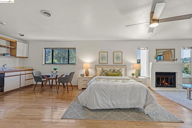 bedroom featuring sink, ceiling fan, light wood-type flooring, a textured ceiling, and a fireplace