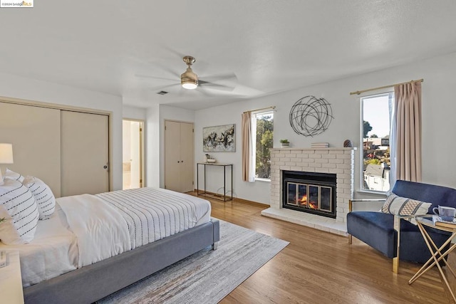 bedroom featuring hardwood / wood-style floors, ceiling fan, and a brick fireplace