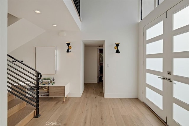 entryway with french doors, light hardwood / wood-style floors, and a high ceiling