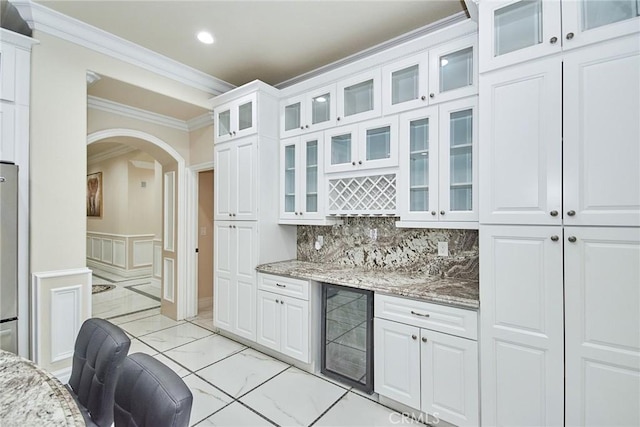 kitchen with light stone countertops, crown molding, white cabinets, and beverage cooler