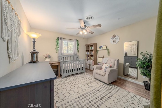 bedroom featuring ceiling fan, a nursery area, and wood-type flooring