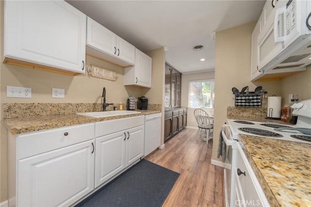 kitchen featuring light stone countertops, white appliances, white cabinetry, light hardwood / wood-style floors, and sink