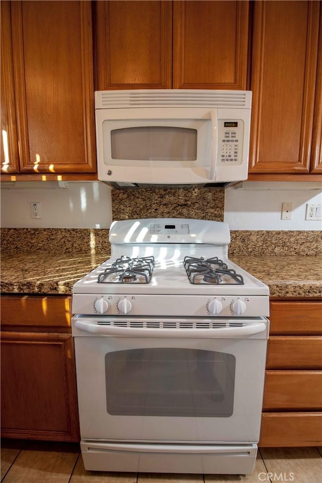 kitchen featuring light tile patterned flooring, light stone counters, and white appliances