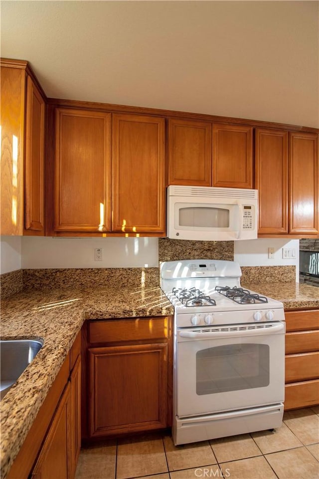 kitchen featuring sink, light tile patterned floors, stone countertops, and white appliances