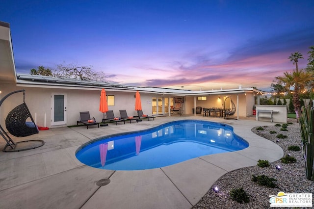 pool at dusk with a patio, area for grilling, and an outdoor bar