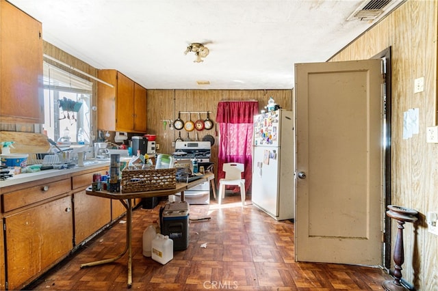 kitchen featuring stainless steel gas range oven, wooden walls, dark parquet floors, and white refrigerator