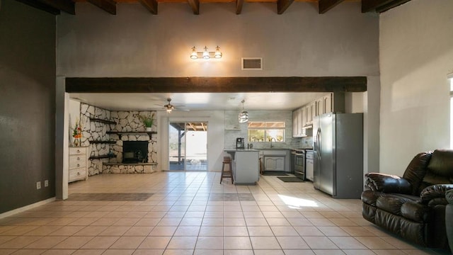 tiled living room with beam ceiling, a stone fireplace, ceiling fan, and sink