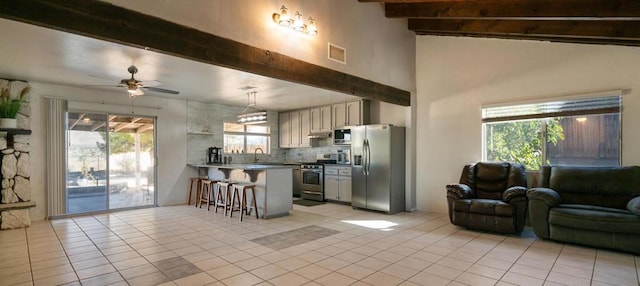 kitchen featuring a breakfast bar, appliances with stainless steel finishes, plenty of natural light, and beamed ceiling