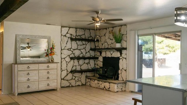 tiled living room featuring a stone fireplace and ceiling fan